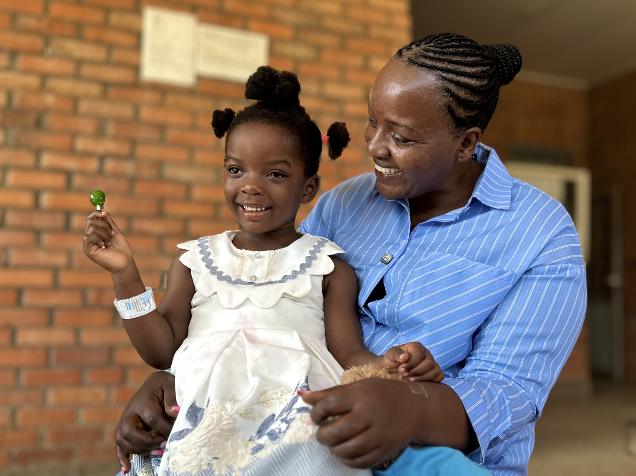 An adult and a small child smiling together sitting outside a brick building