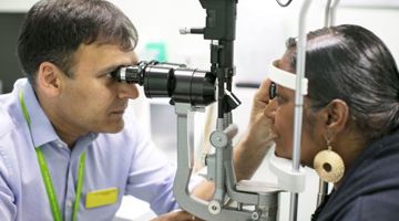 Consultant using optical equipment to look in a patient's eye