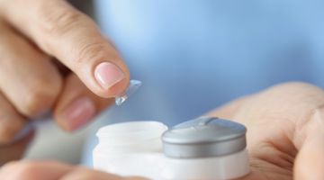 Image of a hand placing a contact lens in it's storage case.