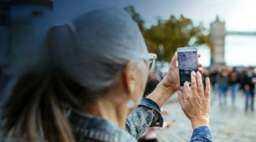 A mature woman taking a photo of a Tower Bridge