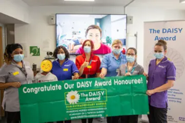 A small group of Moorfields nurses wearing face masks holding the Daisy Award banner