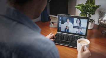 A person talking to people on his laptop and holding a cup of tea
