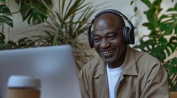 A senior man in headphones looking at his laptop screen and smiling