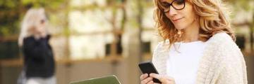 Image of a person sitting on a park bench looking at her tablet and laptop.