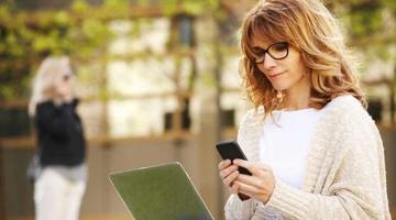 A woman sitting outside with her laptop and phone