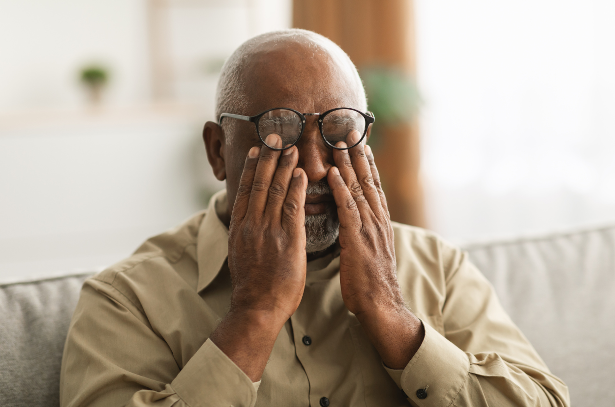 A mature man covering his eyes under his glasses